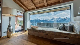 Gemütlicher Wohnbereich mit großer Fensterfront, Holzbalkendecke und atemberaubendem Bergblick.