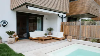 Moderne Terrasse mit bequemen Loungemöbeln, kleinem Pool und EV-Ladestation an der Hauswand.