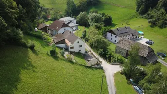 Weitläufige Luftaufnahme einer ländlichen Siedlung, eingebettet in grüne Hügel und Wälder.