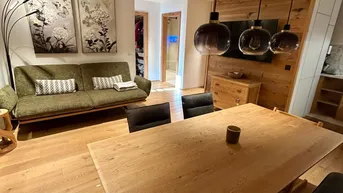 Geräumiger Wohn-Essbereich mit Holzboden, gemütlichem Sofa und modernem Esstisch unter stilvollen Pendelleuchten.