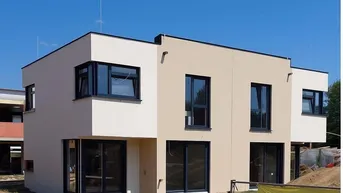 Modernes Reihenhaus im Bau mit großen Fenstern und heller Fassade unter blauem Himmel.