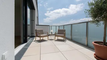 Geräumige Terrasse mit modernen Fliesen, Glasgeländer und bequemen Sitzgelegenheiten unter blauem Himmel.