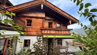 Traditionelles Holzhaus im alpinen Stil mit verzierten Balkonen und grüner Markise.