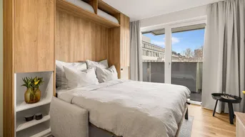 Helles Schlafzimmer mit integriertem Schrankbett, Holzelementen und Zugang zum Balkon.