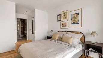 Helles Schlafzimmer mit Holzboden, modernem Bett und Zugang zu einem Ankleidebereich mit Bad.