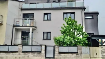 Modernes Mehrfamilienhaus mit Balkonen und Dachterrasse, umgeben von einer Steinmauer.
