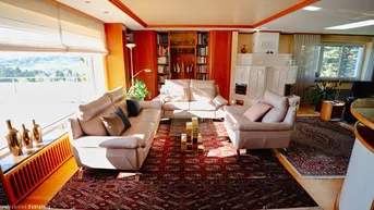 Geräumiges Wohnzimmer mit Kachelofen, bequemen Sofas und Blick auf die grüne Umgebung.
