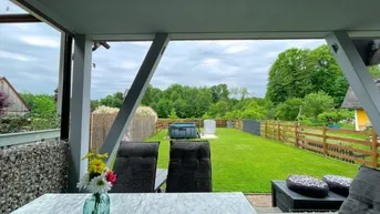 Überdachte Terrasse mit Sitzgelegenheiten und Blick auf den grünen Garten mit kleinem Pool.