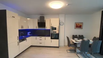 Moderne Küche mit integriertem Essbereich, glänzenden Fronten und blauer Akzentbeleuchtung.