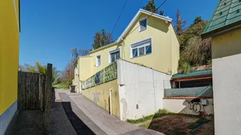 Gelbes Haus von der Seite mit Zugangsweg und angrenzendem Hang.