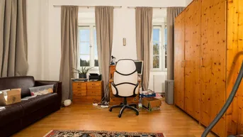 Geräumiges Wohnzimmer mit Holzboden, großem Kleiderschrank und Arbeitsbereich am Fenster.