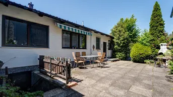 Große gepflasterte Terrasse mit Gartenmöbeln und Markise, umgeben von viel Grün.