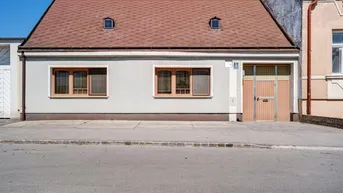 Vorderansicht eines Einfamilienhauses mit Satteldach und kleinen Dachgauben an einem sonnigen Tag.