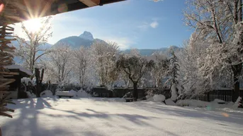 Verschneiter Garten mit Blick auf die Berge an einem sonnigen Wintertag, umgeben von Bäumen.