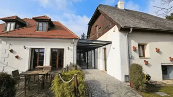 Charmantes Gebäudeensemble mit Terrasse und Zugang über eine Rampe, umgeben von Grünflächen.