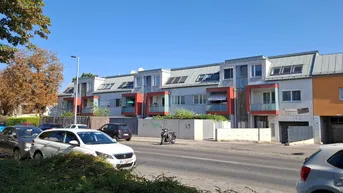 Moderne Reihenhäuser mit orangefarbenen Akzenten und Schrägdächern entlang einer ruhigen Wohnstraße.