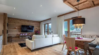 Gemütlicher Wohn-Essbereich mit Holzwand, modernem Sofa und rustikalem Esstisch, bietet direkten Balkonzugang.