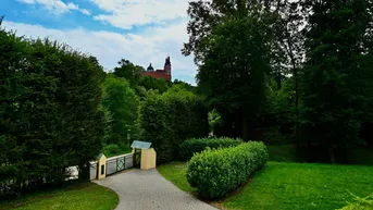 Blick auf ein entferntes historisches Gebäude, umgeben von üppigem Grün und einem gepflegten Eingangstor.
