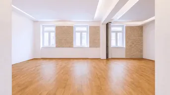 Helles, leeres Wohnzimmer mit Holzboden, freiliegender Ziegelwand und großen Fenstern.