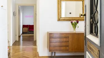 Heller Flur mit Fischgrätparkett, einem antiken Sideboard und einem vergoldeten Spiegelrahmen.