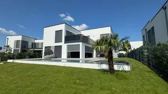 Moderne Villa mit Swimmingpool und gepflegtem Rasen unter blauem Himmel.