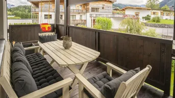 Gemütlicher Balkon mit Holztisch, Sitzgelegenheiten und Blick auf die umliegenden Häuser.