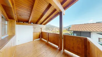 Geräumiger Holzbalkon mit freiem Blick auf die umliegende Berglandschaft und viel Sonnenlicht.