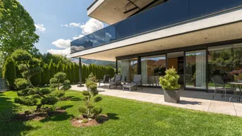 Moderne Villa mit großer Terrasse, Garten und gepflegter Rasenfläche unter blauem Himmel.