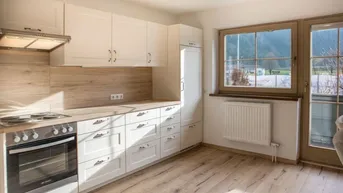 Helle Küche mit weißen Schränken, Holzoptik-Arbeitsplatte und Blick ins Grüne.