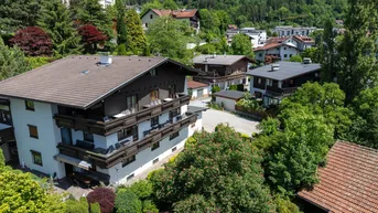 Luftaufnahme eines Mehrfamilienhauses mit mehreren Balkonen, umgeben von üppiger Vegetation und anderen Gebäuden.