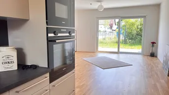 Moderne Einbauküche mit integrierten Geräten und Blick auf den Garten durch die große Schiebetür.