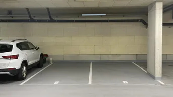 Helle Tiefgarage mit markierten Parkplätzen und Betonwänden, ein Fahrzeug ist bereits geparkt.