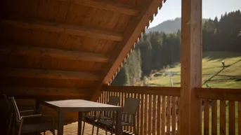 Überdachter Holzbalkon mit Sitzgelegenheiten und weitem Blick auf die grüne Berglandschaft.