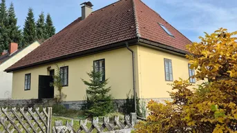 Gelbes Landhaus mit rotem Ziegeldach und Holzzaun in ländlicher Umgebung.