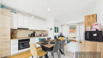 Heller offener Wohn- und Essbereich mit integrierter Küche, Holzboden und Zugang zum Balkon.