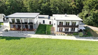 Luftaufnahme von zwei modernen Häusern mit Gärten und umgeben von Wald.