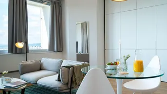 Helles, modernes Wohnzimmer mit bequemer Couch, Esstisch und großen Fenstern.