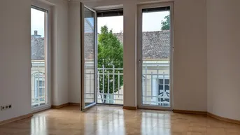 Helles Zimmer mit Parkettboden und Zugang zu einem französischen Balkon mit Blick auf die Straße.
