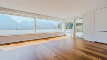 Helles Wohnzimmer mit großen Fenstern, Holzboden und beeindruckendem Bergblick.