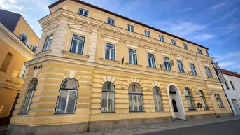 Gelbes historisches Gebäude mit klassischer Architektur und "HOTEL"-Beschriftung unter blauem Himmel.