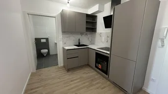 Moderne Küchenzeile mit grauen Fronten, Marmoroptik-Rückwand und Blick in ein separates WC.