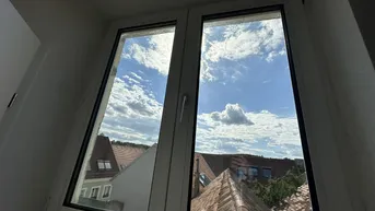 Blick aus dem Fenster auf die Dächer der umliegenden Gebäude und den blauen Himmel.