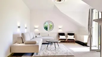 Helles Wohnzimmer mit gemütlichem Sofa, runden Fenstern und Zugang zum Balkon.