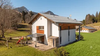 Modernes Haus mit weißer Fassade, Holzverkleidung, überdachter Terrasse und Bergblick.