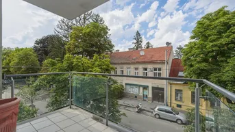 Geräumiger Balkon mit Glasgeländer bietet einen Blick auf die Straße und umliegende Gebäude.