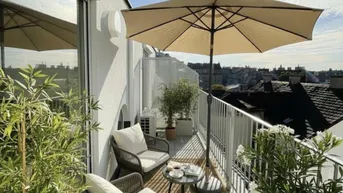 Sonniger Balkon mit bequemen Sitzgelegenheiten, Pflanzen und Blick über die Dächer der Stadt.