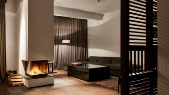 Gemütliches Wohnzimmer mit modernem Kamin, dunklem Sofa und Holzboden.