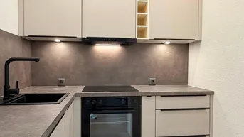 Moderne Einbauküche mit hellen Schränken, integriertem Backofen und Induktionskochfeld.