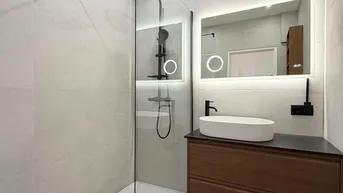 Modernes Badezimmer mit ebenerdiger Dusche, beleuchtetem Spiegel und elegantem Waschtischunterschrank.