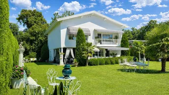 Weitläufiger Garten mit gepflegtem Rasen, Palmen und eleganten Sitzgelegenheiten vor dem Haus.